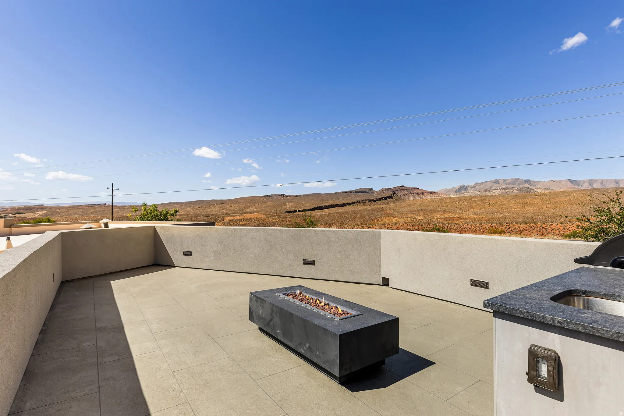 Spacious outdoor terrace featuring large format tile flooring, a built-in fire pit, and an outdoor kitchen with a stone countertop and integrated sink