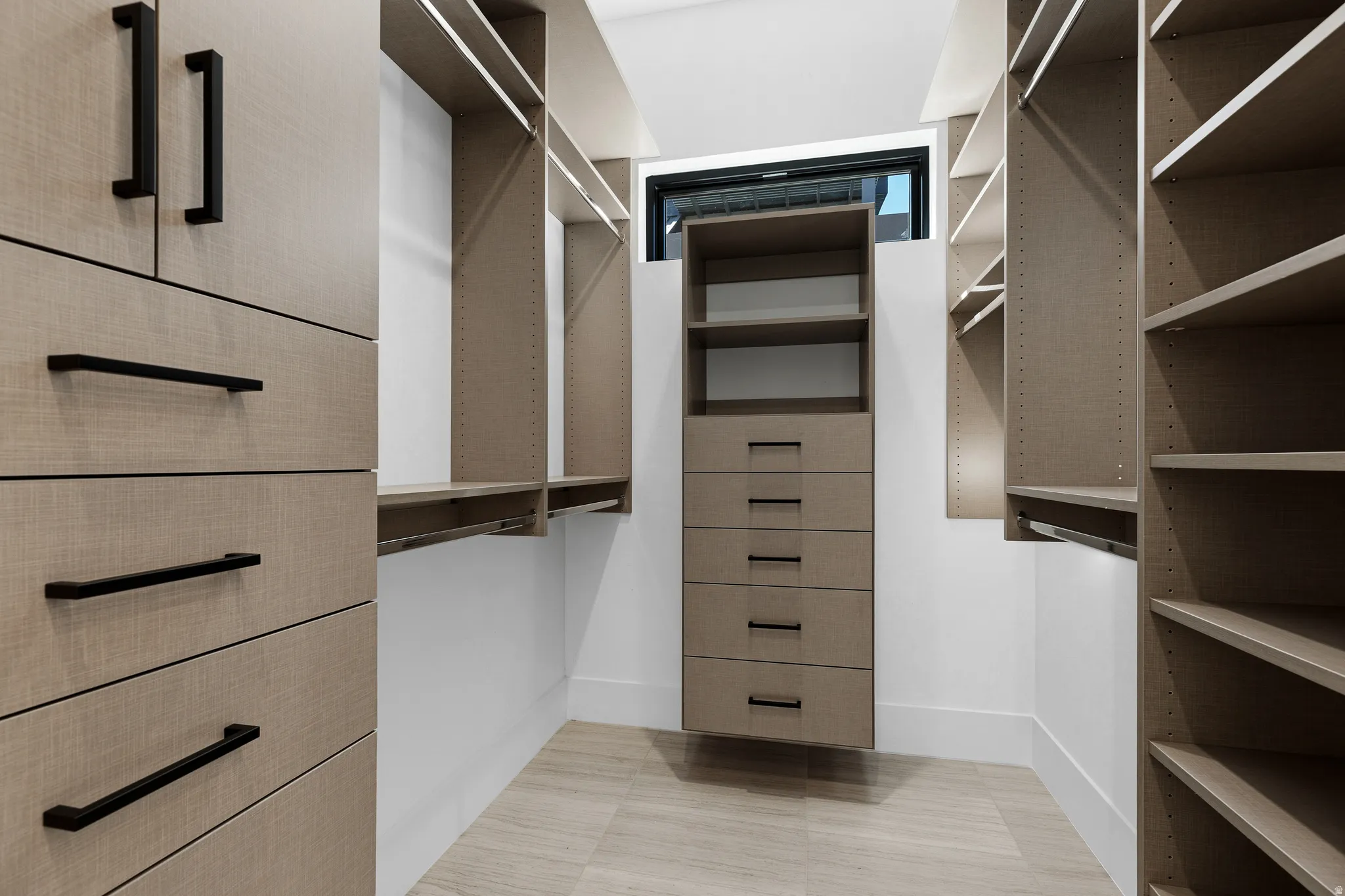 Walk-in closet featuring light wood-finish cabinetry, black hardware, integrated shelving, drawer storage, and a transom window