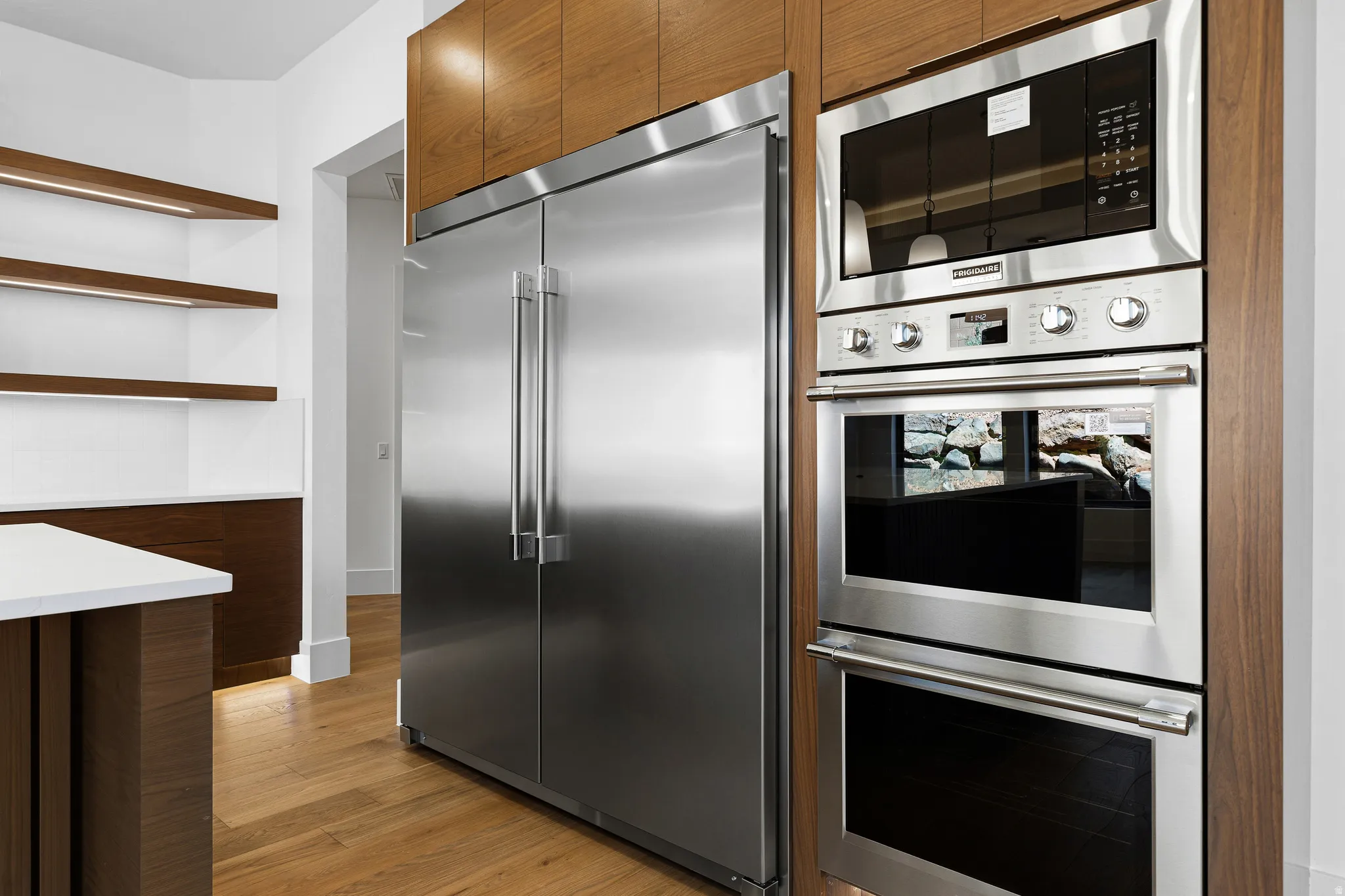 Integrated stainless steel refrigerator, built-in microwave, and double wall ovens set within wood-finish cabinetry