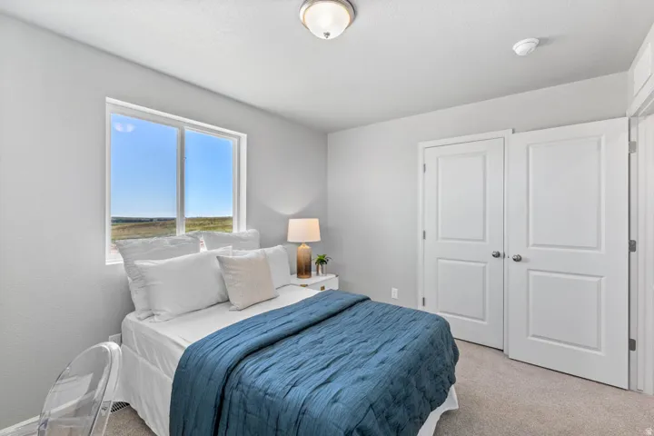 Bright bedroom featuring a large window, carpet flooring, a ceiling-mounted light fixture, and two panel doors