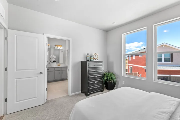 Carpeted bedroom featuring two large windows, a light gray wall finish, and a door leading to a bathroom with a gray vanity