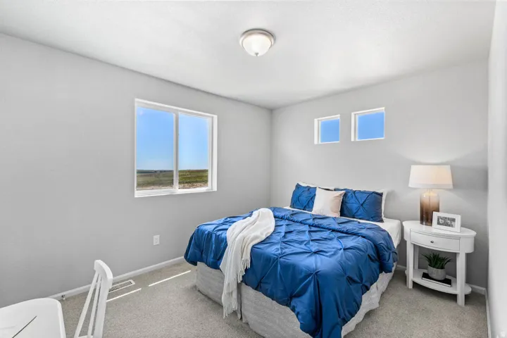 Bedroom featuring light gray walls, carpet flooring, a large window, and two smaller upper windows providing natural illumination