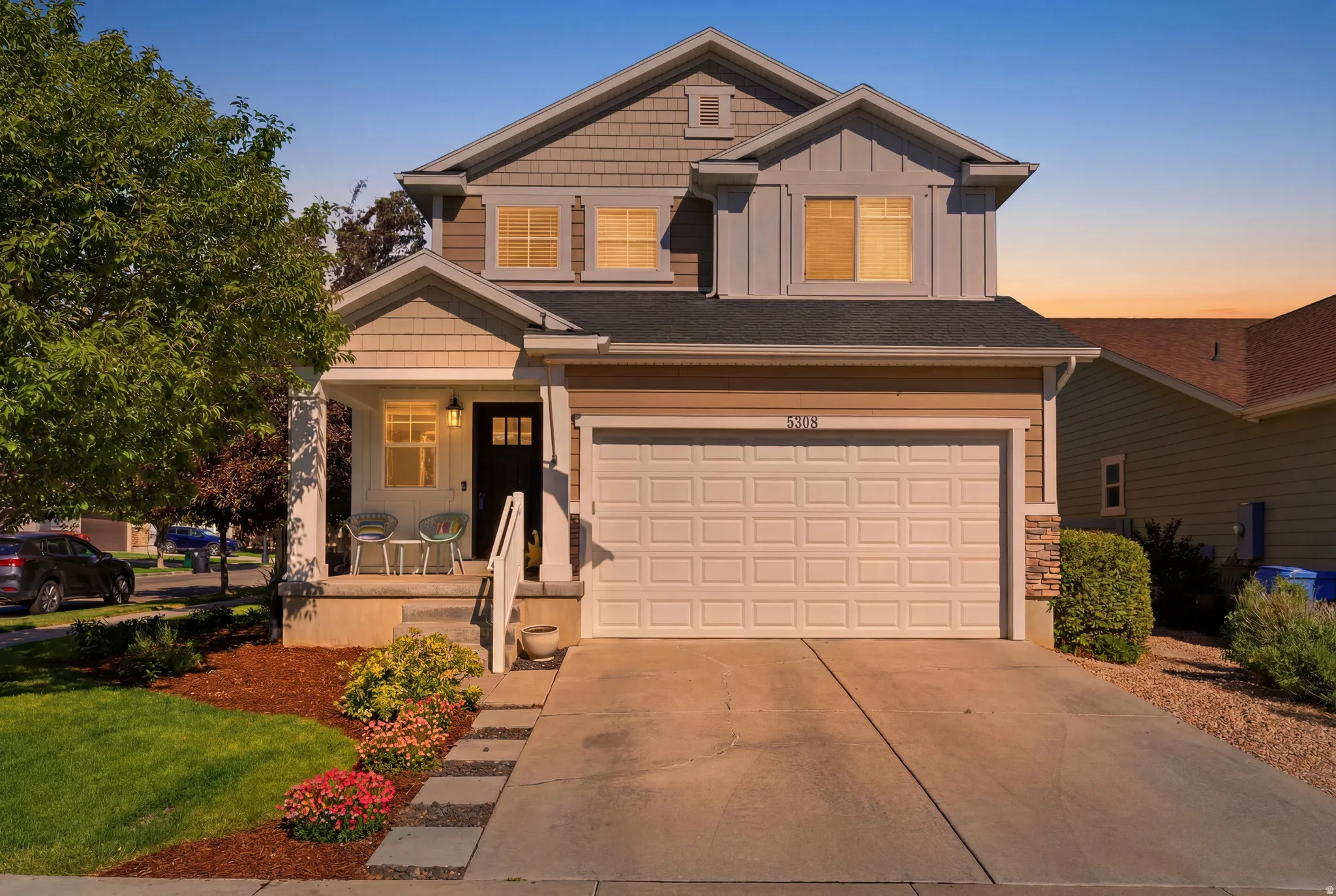 Two-story residence featuring a covered front porch, an attached two-car garage, and a multi-textured facade with horizontal siding, shaker siding, and stone accents