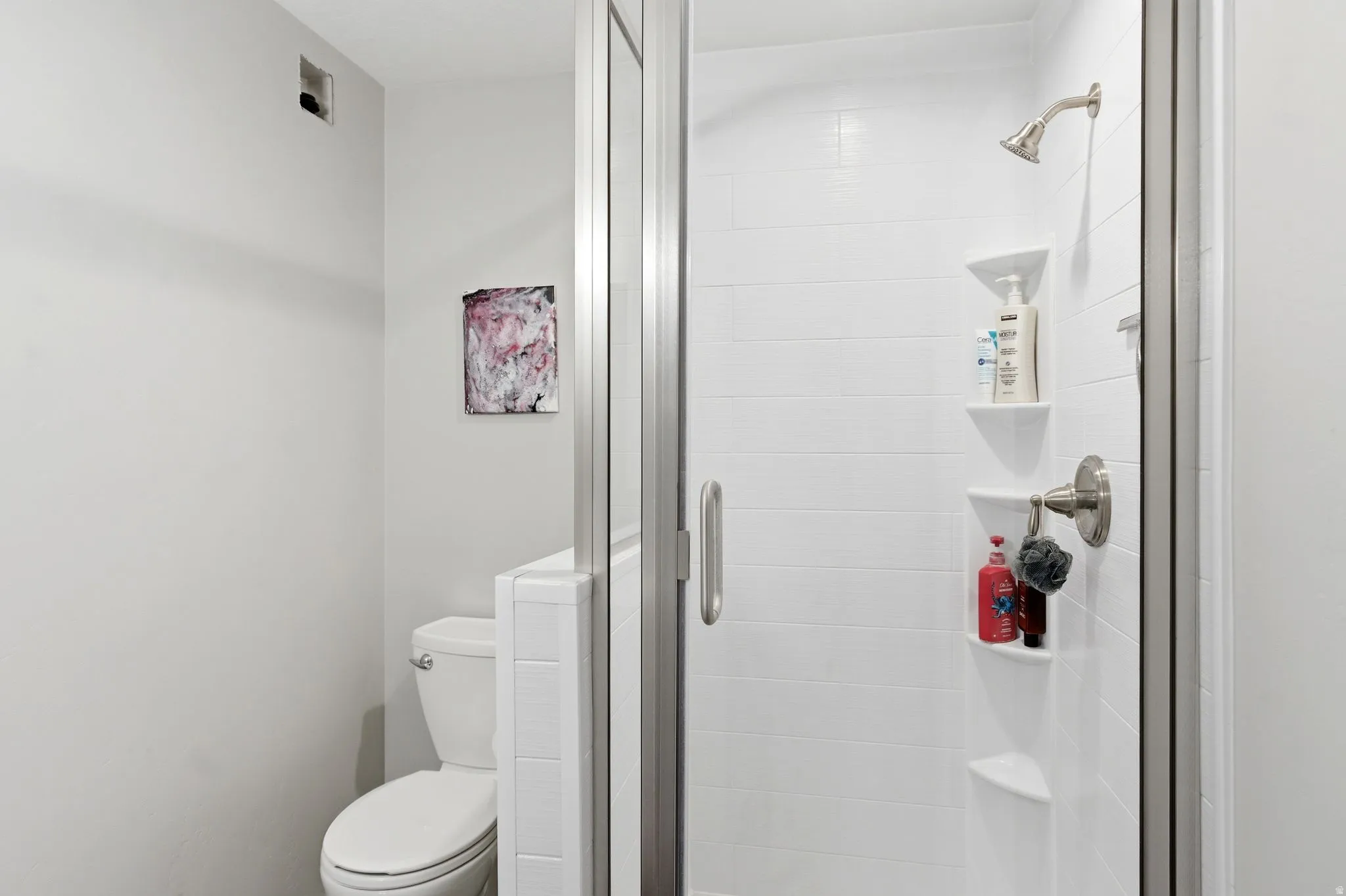 Glass-enclosed shower featuring white subway tile, a brushed nickel showerhead, and integrated shelving