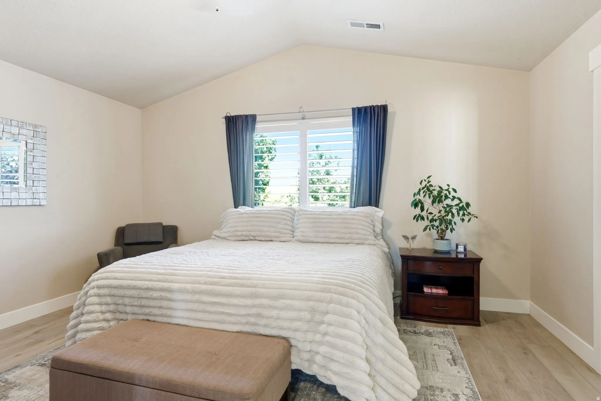 Bedroom featuring vaulted ceilings, light wood-finish flooring, and a large window with plantation shutters
