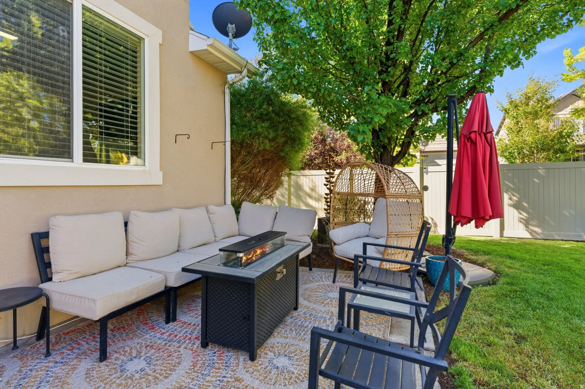 Paved outdoor patio featuring a built-in fire pit, surrounded by lush green lawn and mature trees