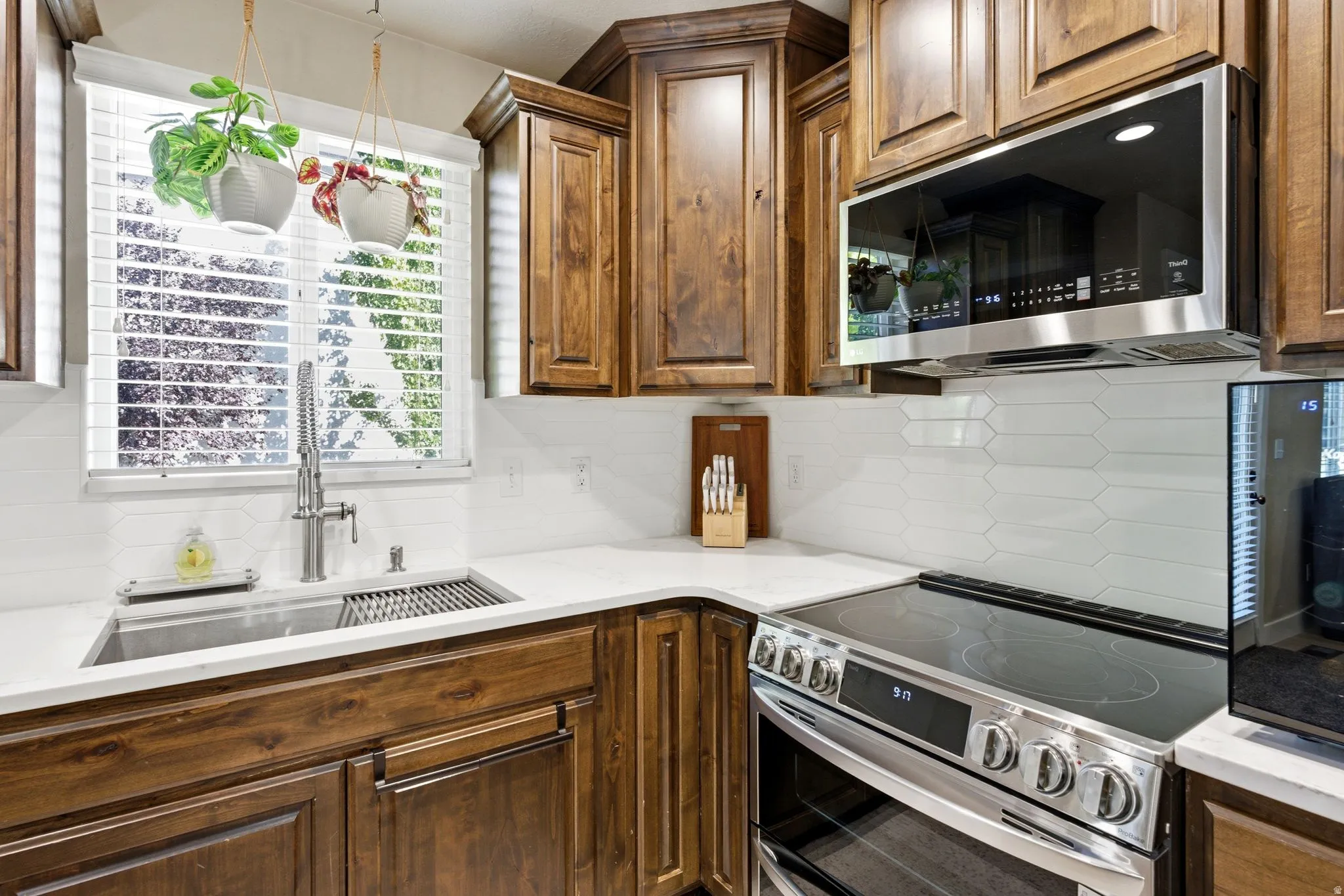 Kitchen featuring a stainless steel undermount sink, gooseneck faucet, quartz countertops, white picket tile backsplash, and wood cabinetry