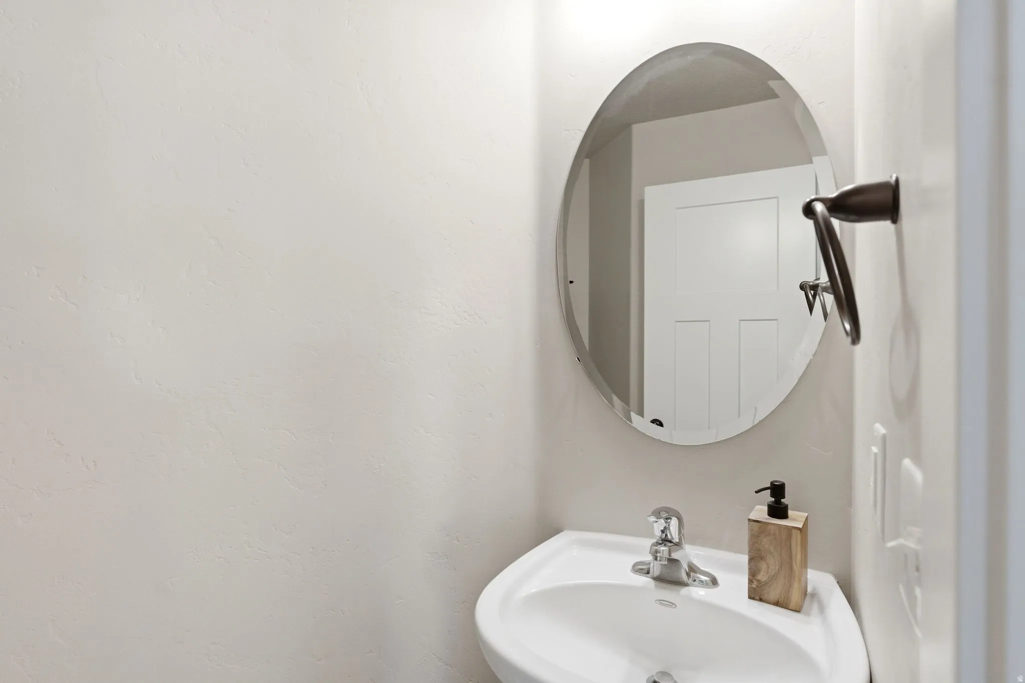 Pedestal sink with chrome faucet, complemented by an oval-shaped mirror