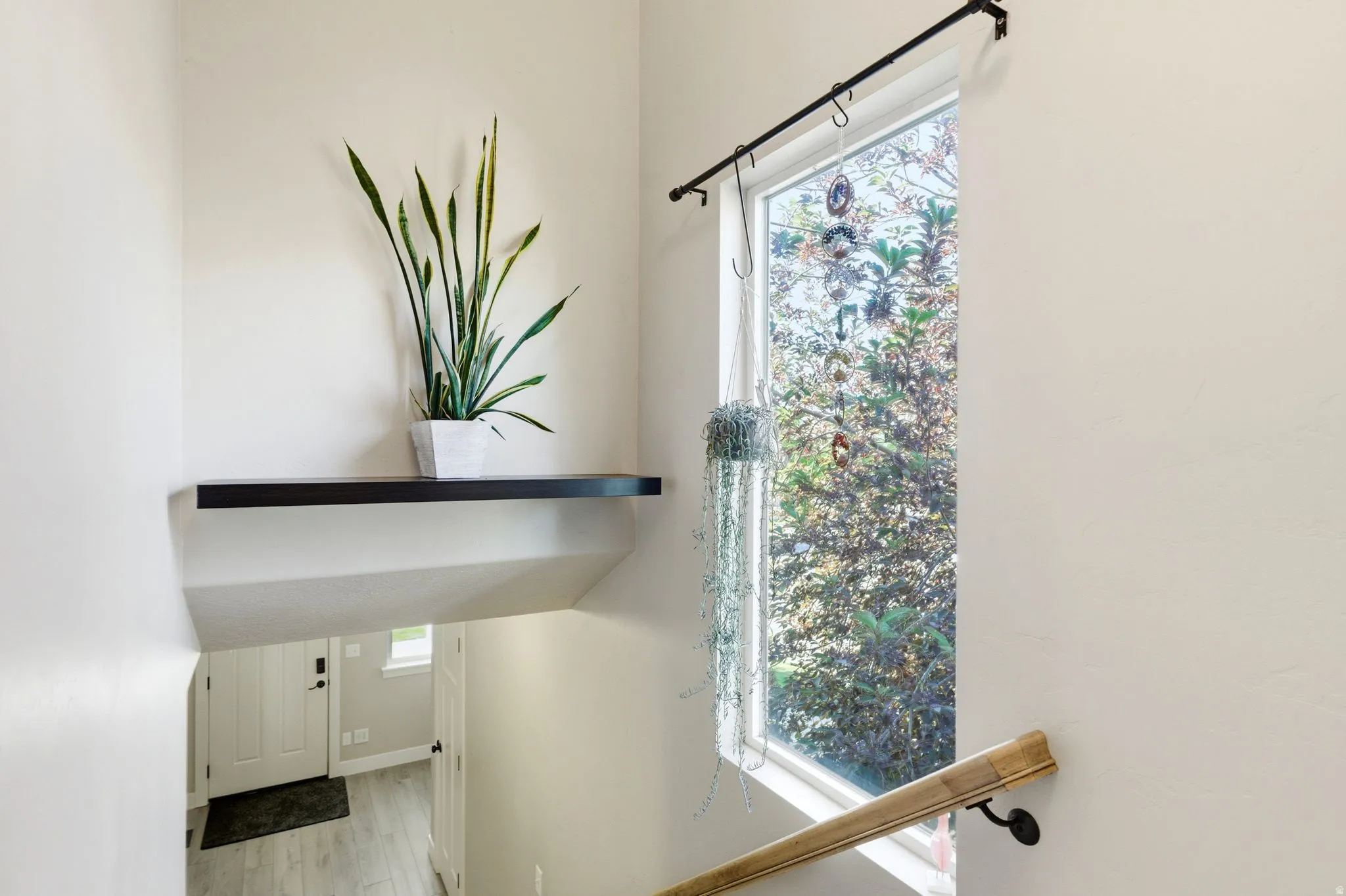 Stairwell featuring a prominent vertical window, natural wood handrail, and a black floating shelf