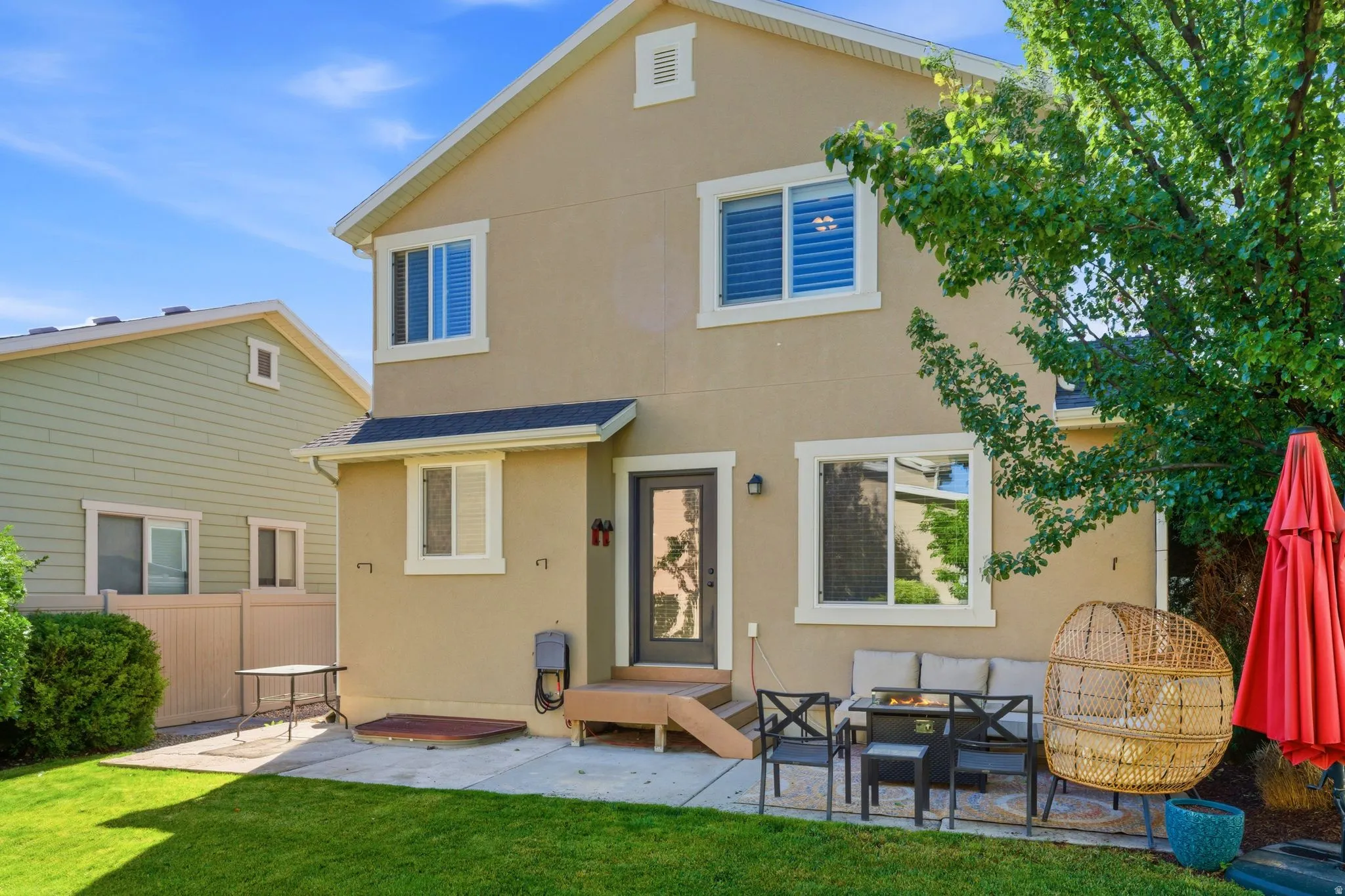 Rear exterior featuring a tan stucco finish, white trim windows, a paved patio area, and a green lawn