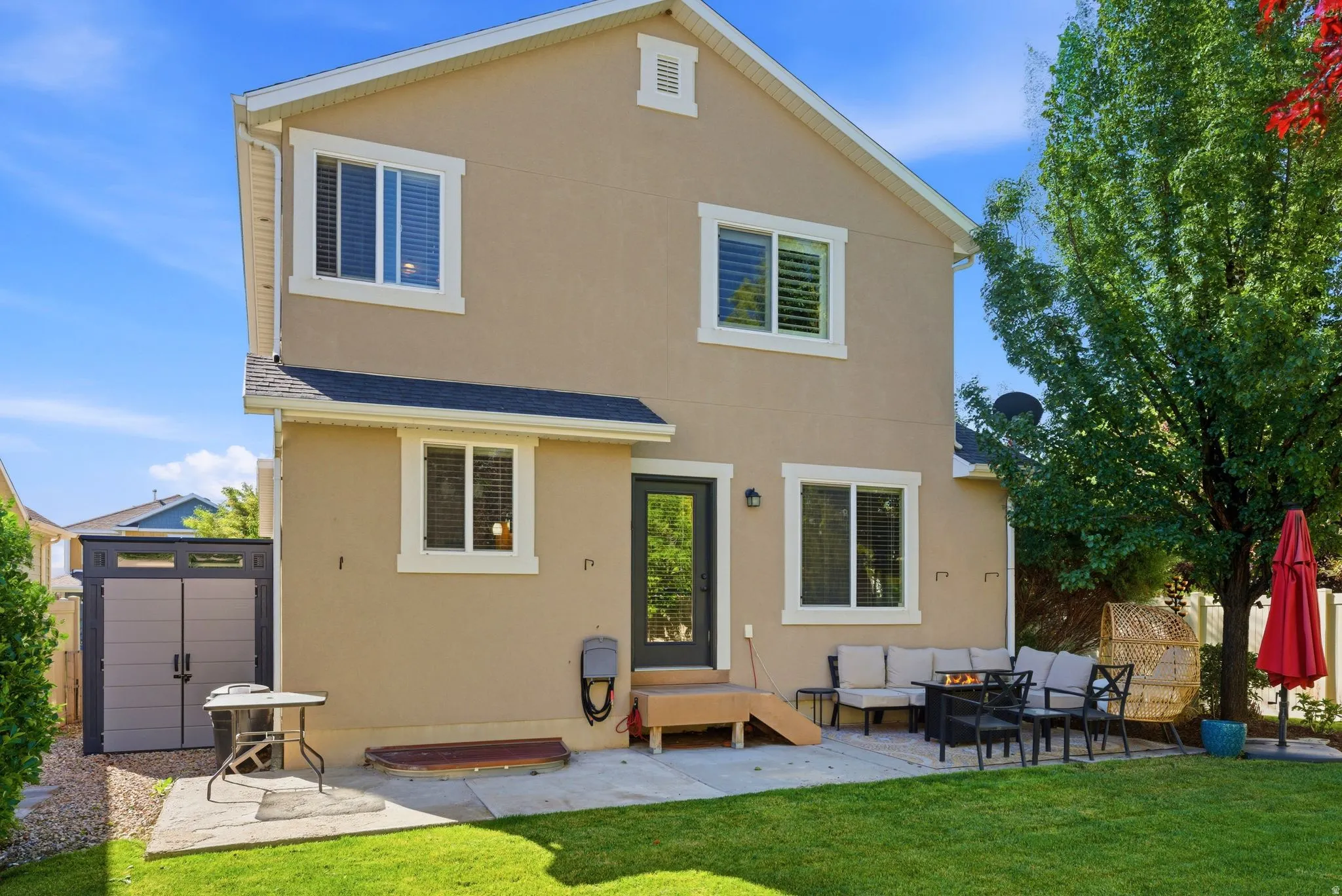 Rear exterior featuring a tan stucco finish, white trim windows, and a black roof