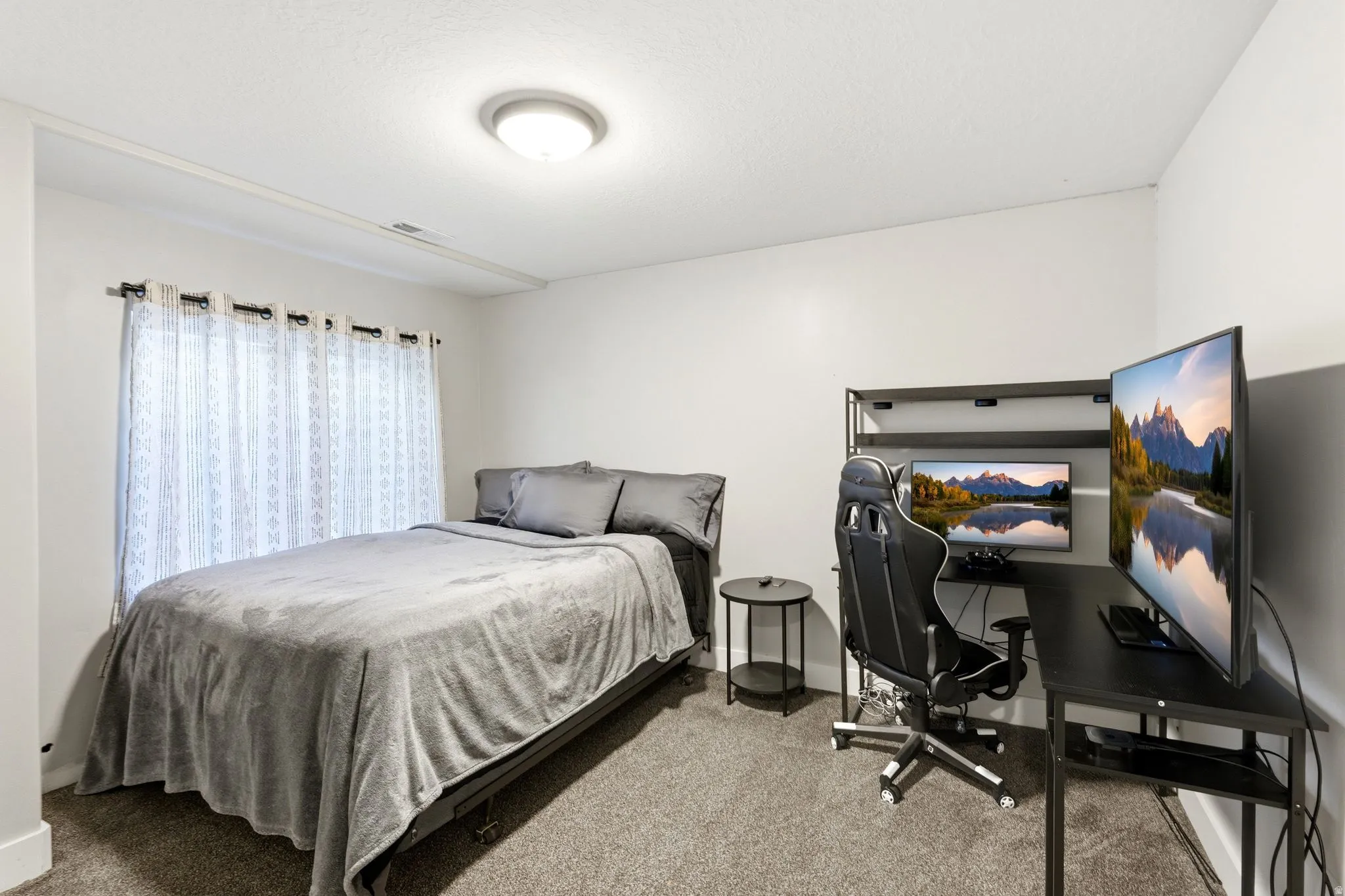 Carpeted room featuring a window with patterned curtains, white walls, and a ceiling-mounted light fixture