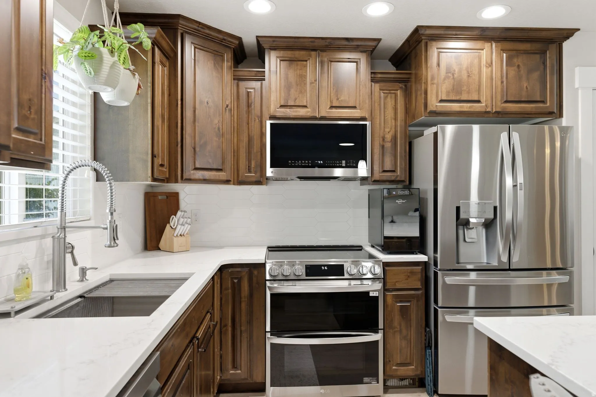 Kitchen featuring custom wood cabinetry, stainless steel appliances, white countertops, and a white subway tile backsplash