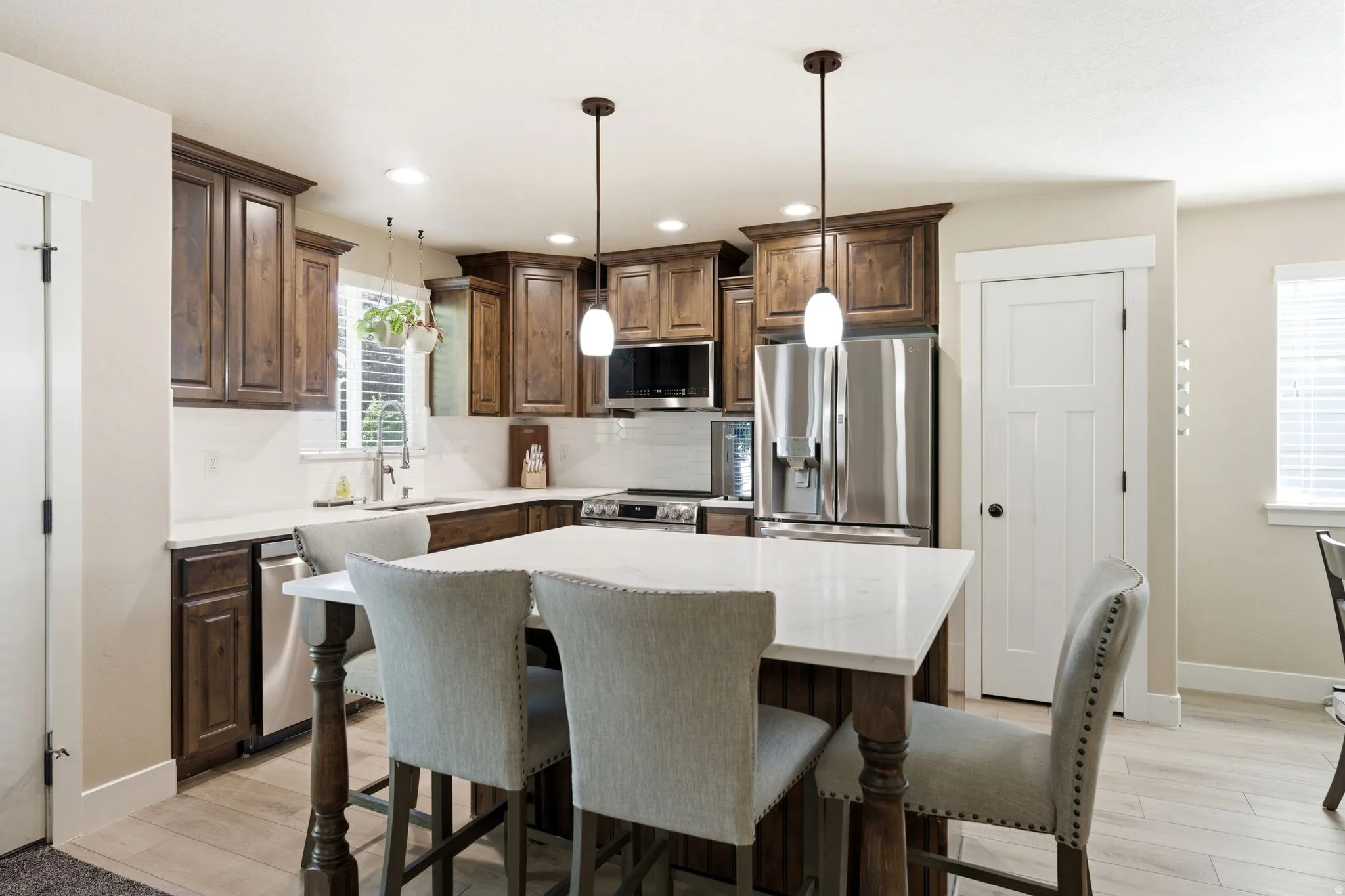 Spacious kitchen featuring an expansive island with seating, rich wood cabinetry, stainless steel appliances, white countertops, and wood-finish flooring