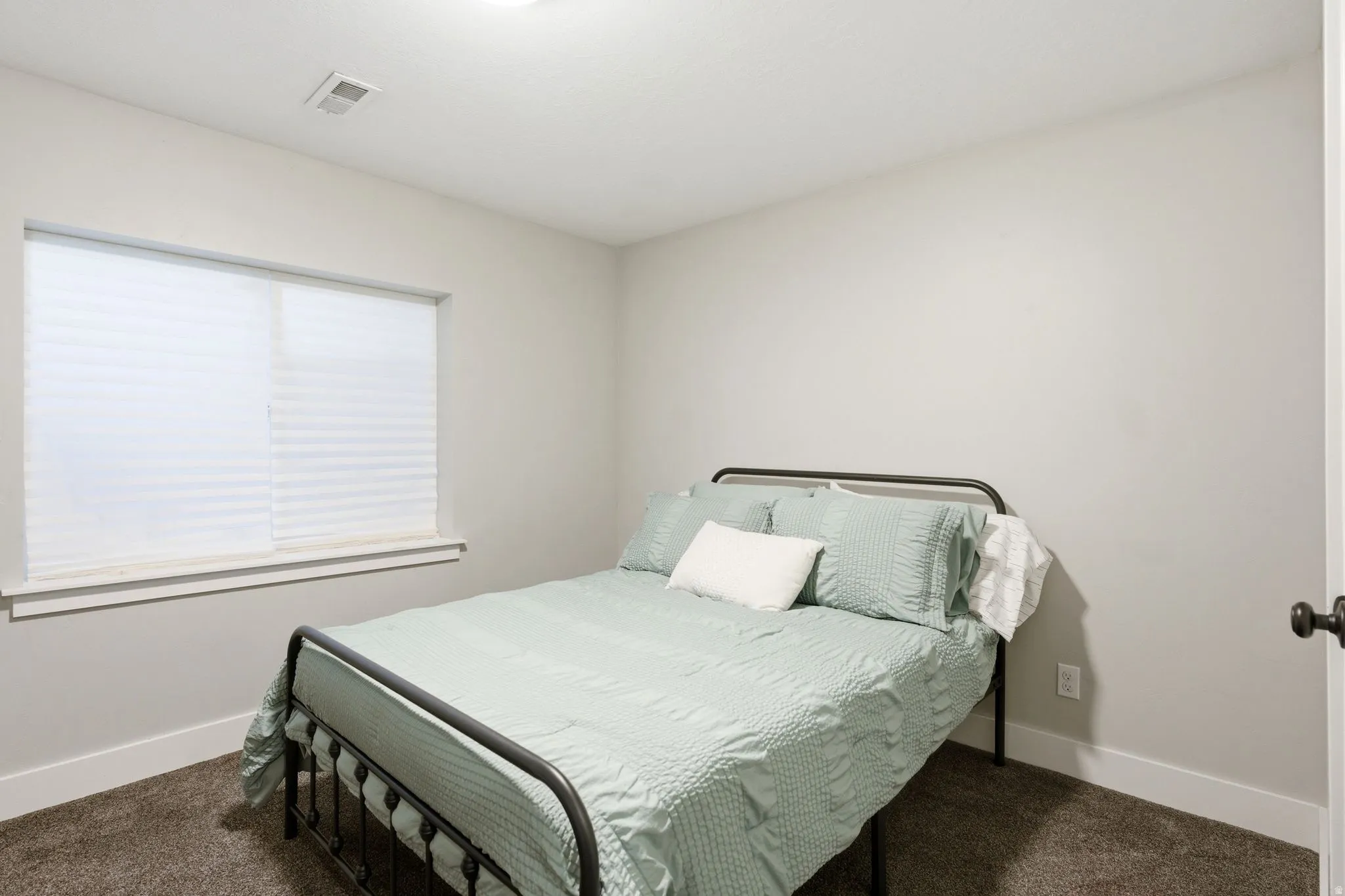 Bedroom featuring light gray wall paint, a window with white blinds, dark carpet flooring, and white baseboards
