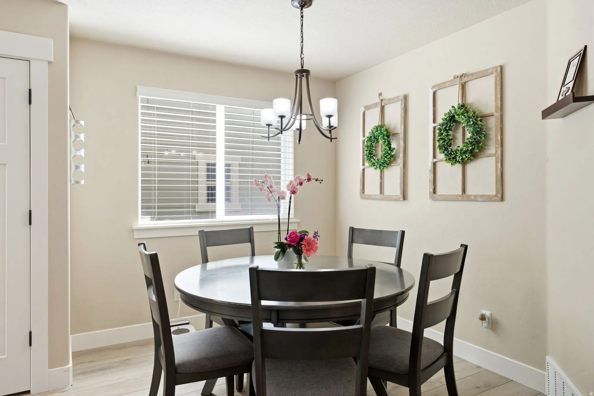 Dining area featuring a window with blinds, a ceiling-mounted chandelier, light-toned walls, wood-finish flooring, and a white interior door