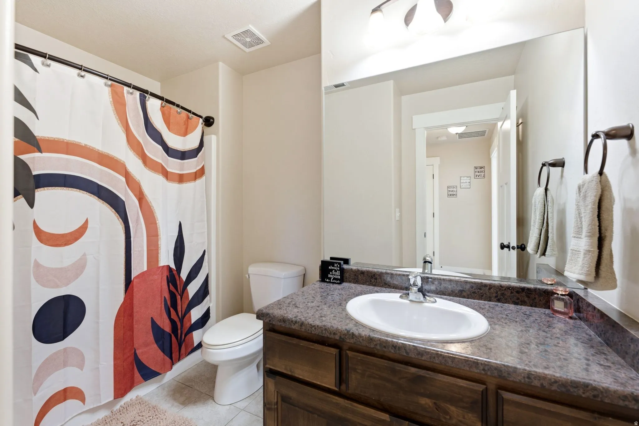 Bathroom featuring a single vanity with wood-finish cabinetry, a white oval sink, and a speckled countertop
