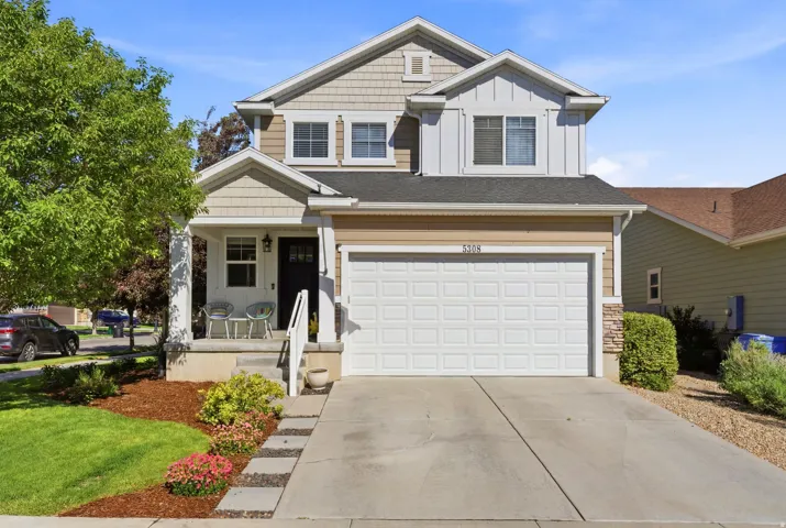 Two-story residence featuring a covered front porch, an attached two-car garage, partial stone façade detailing, and a concrete driveway