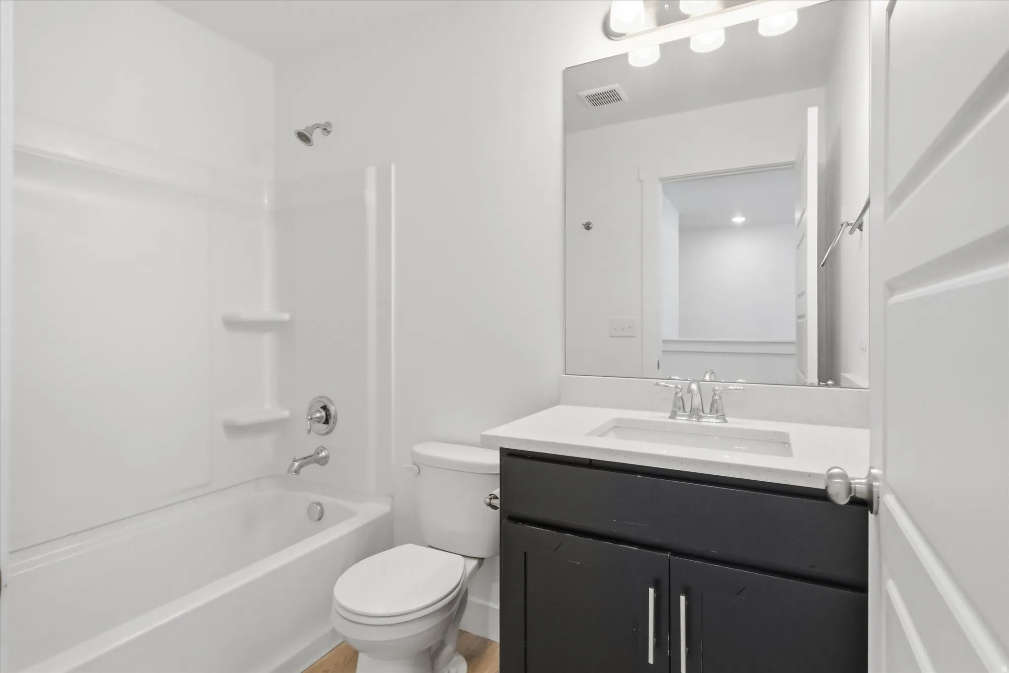 Bathroom featuring a dark wood-finish vanity with a white countertop and undermount sink, a large wall-mounted mirror, and a white tub/shower combination with chrome fixtures