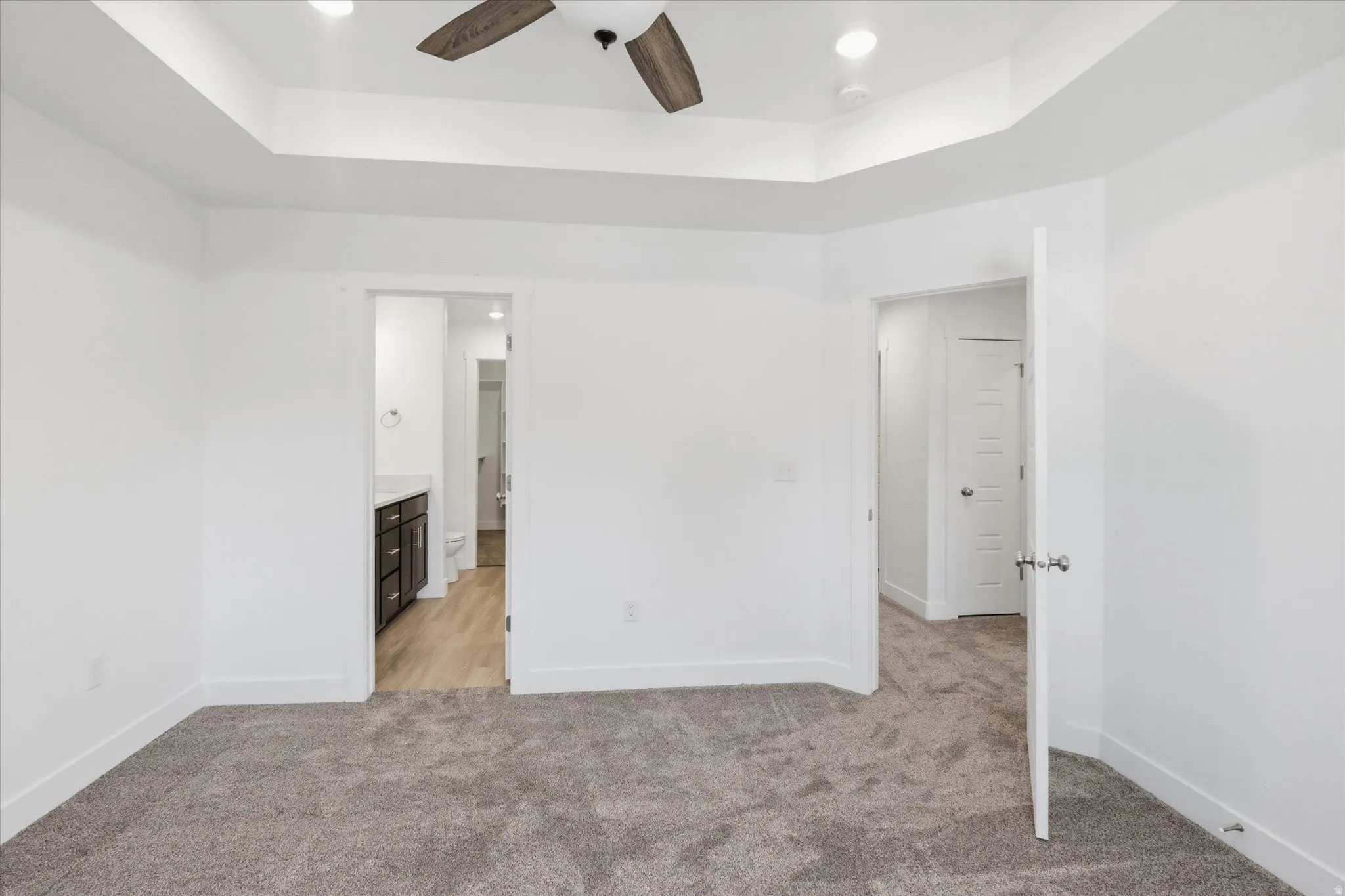 Spacious room featuring tray ceilings, a ceiling fan with wood-finish blades, recessed lighting, and plush grey carpeting