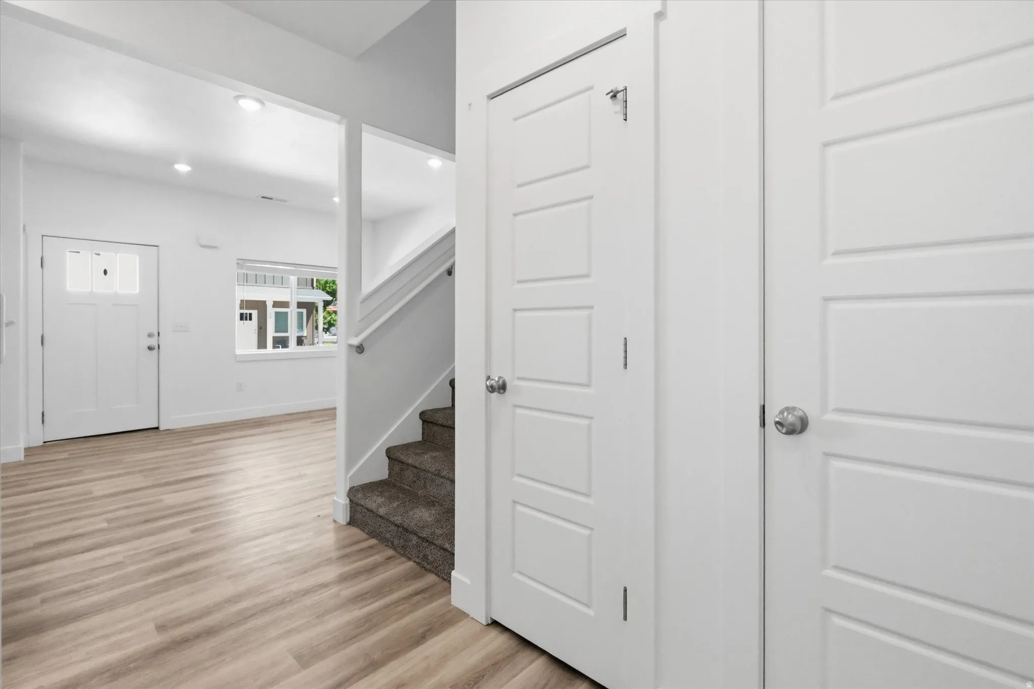 Entryway featuring light wood-finish flooring, white paneled doors, recessed lighting, and a window with white trim