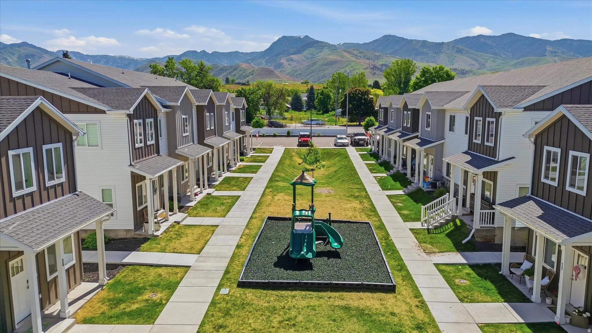 Centralized green space with a playground, framed by modern townhomes featuring covered front porches and distinct siding