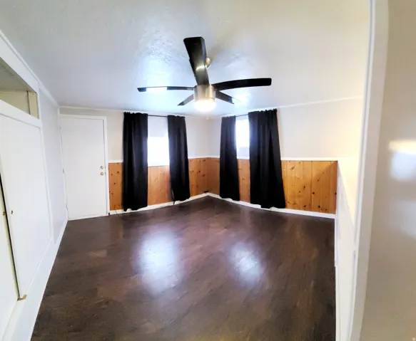 Spacious room featuring rich wood-finish flooring, half-wall wood paneling, and a contemporary ceiling fan with integrated lighting