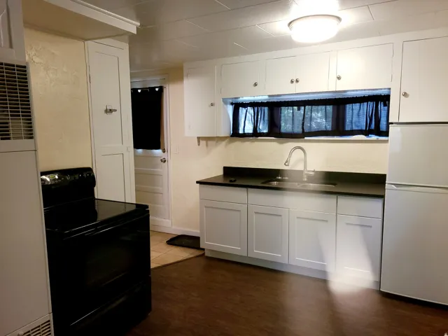 Kitchen featuring white cabinetry, dark countertops, a stainless steel sink with a gooseneck faucet, a white refrigerator, and dark wood-finish flooring