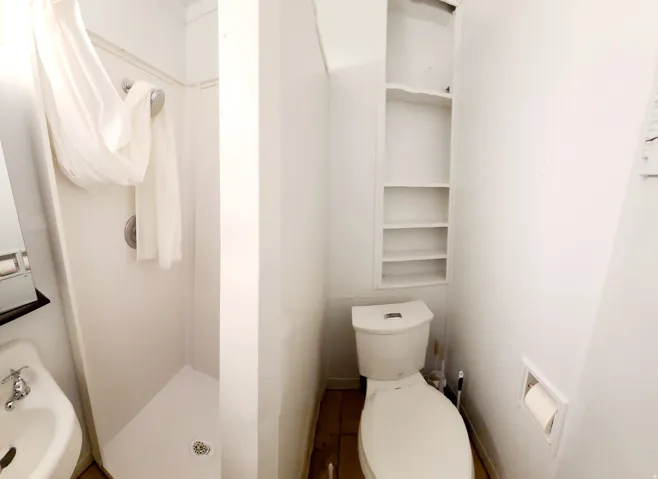 Compact bathroom featuring a stand-up shower with a showerhead, a wall-mounted sink with chrome faucet, a toilet, and built-in shelving