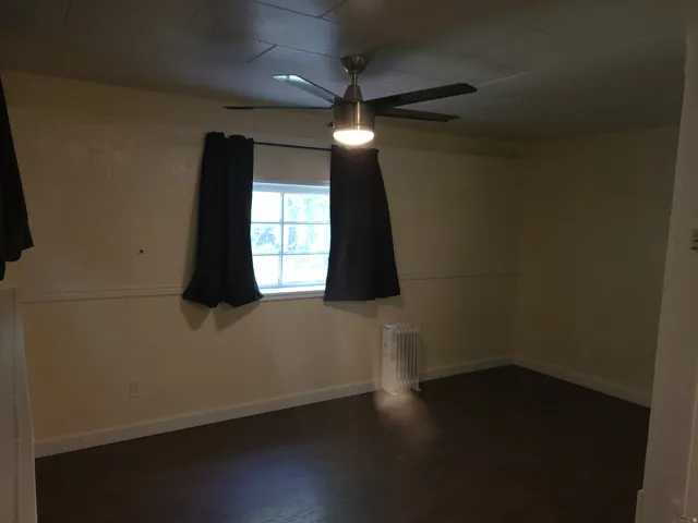 Room featuring dark wood-finish flooring, a ceiling fan with integrated lighting, and a white-framed window
