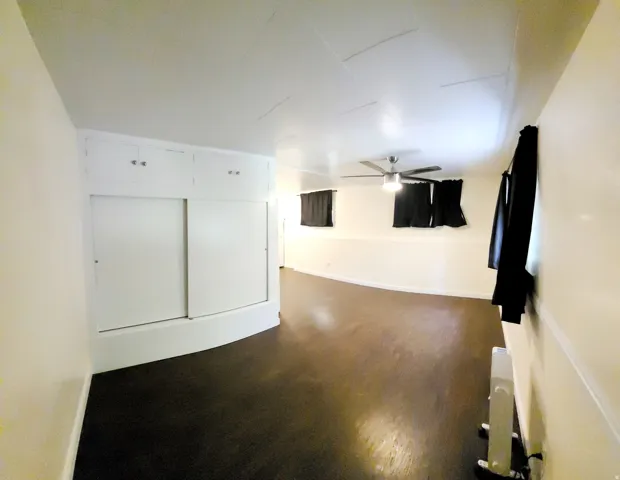 Interior space featuring dark wood-finish flooring, light-colored walls, and a ceiling fan with integrated lighting
