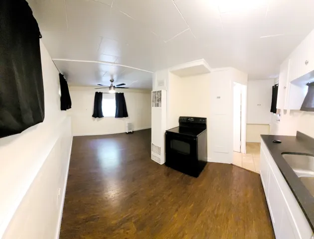 Open-concept living space with wood-finish flooring, a ceiling fan, and a black range