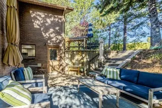 Tiered backyard featuring a brick exterior, concrete patio, built-in wooden stairs, and established trees