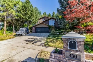 Mid-century modern style residence featuring a two-car garage, expansive driveway, and a stone-clad entry monument with integrated house numbers