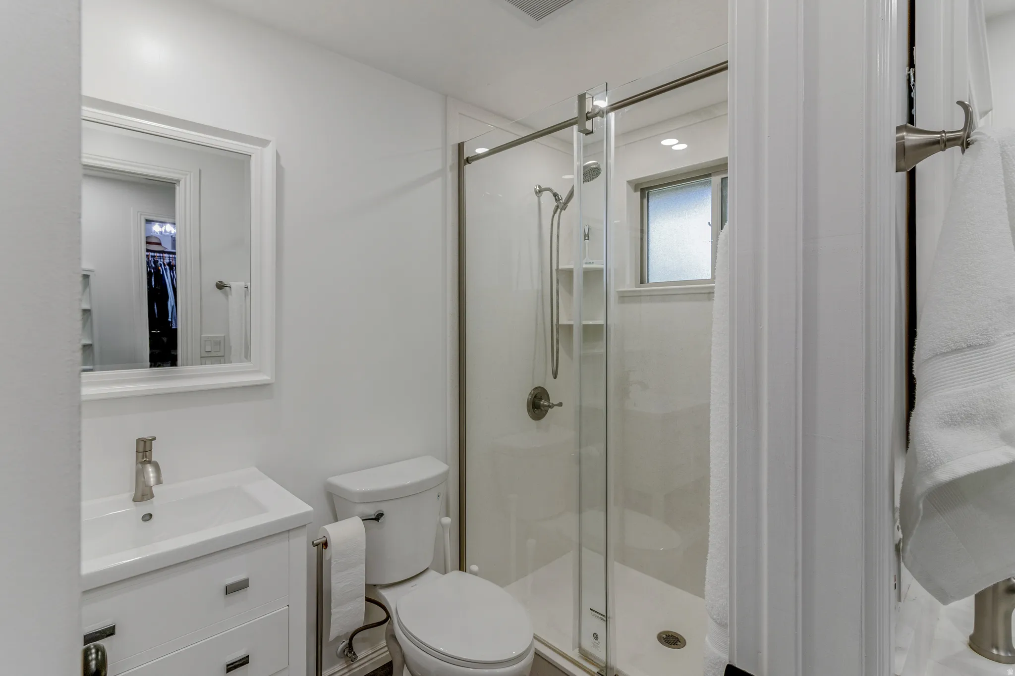 Bright bathroom featuring a glass-enclosed shower with built-in shelving, white vanity with integrated sink, brushed nickel fixtures, and a framed mirror