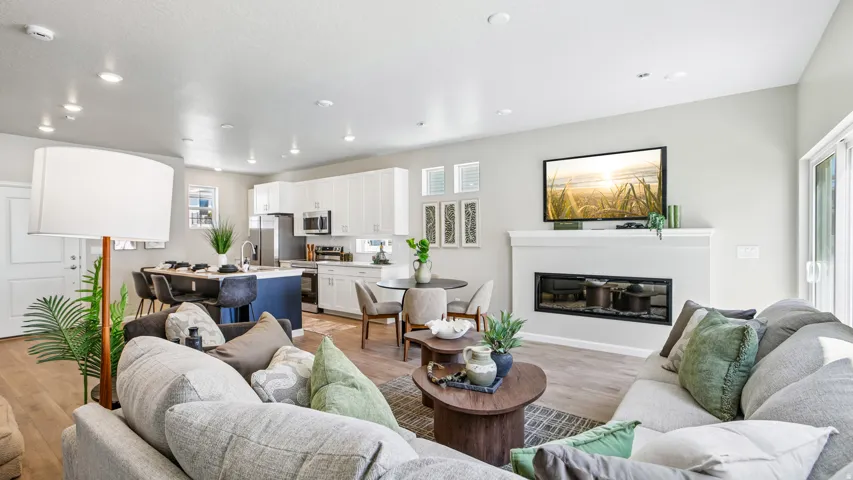 Open-concept living area featuring wood-finish flooring, a contemporary linear fireplace with a mantel, recessed lighting, a kitchen island with seating, and white cabinetry