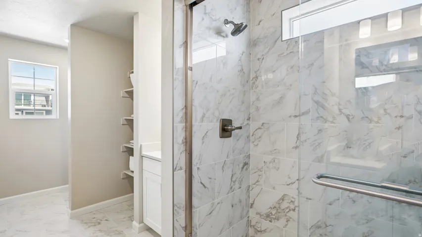 Spacious shower with glass enclosure and light-toned, veined tilework