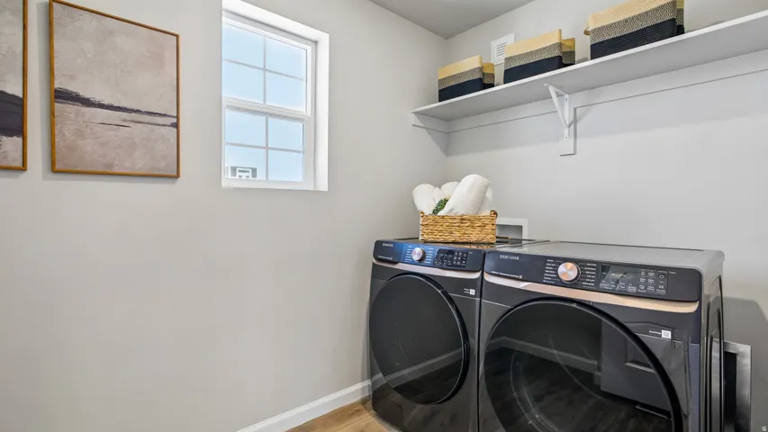 Laundry area featuring a window, wood-finish flooring, two large appliances, white wall shelving, and light gray wall paint