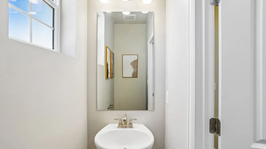 Pedestal sink with a brushed nickel faucet, framed by a rectangular mirror