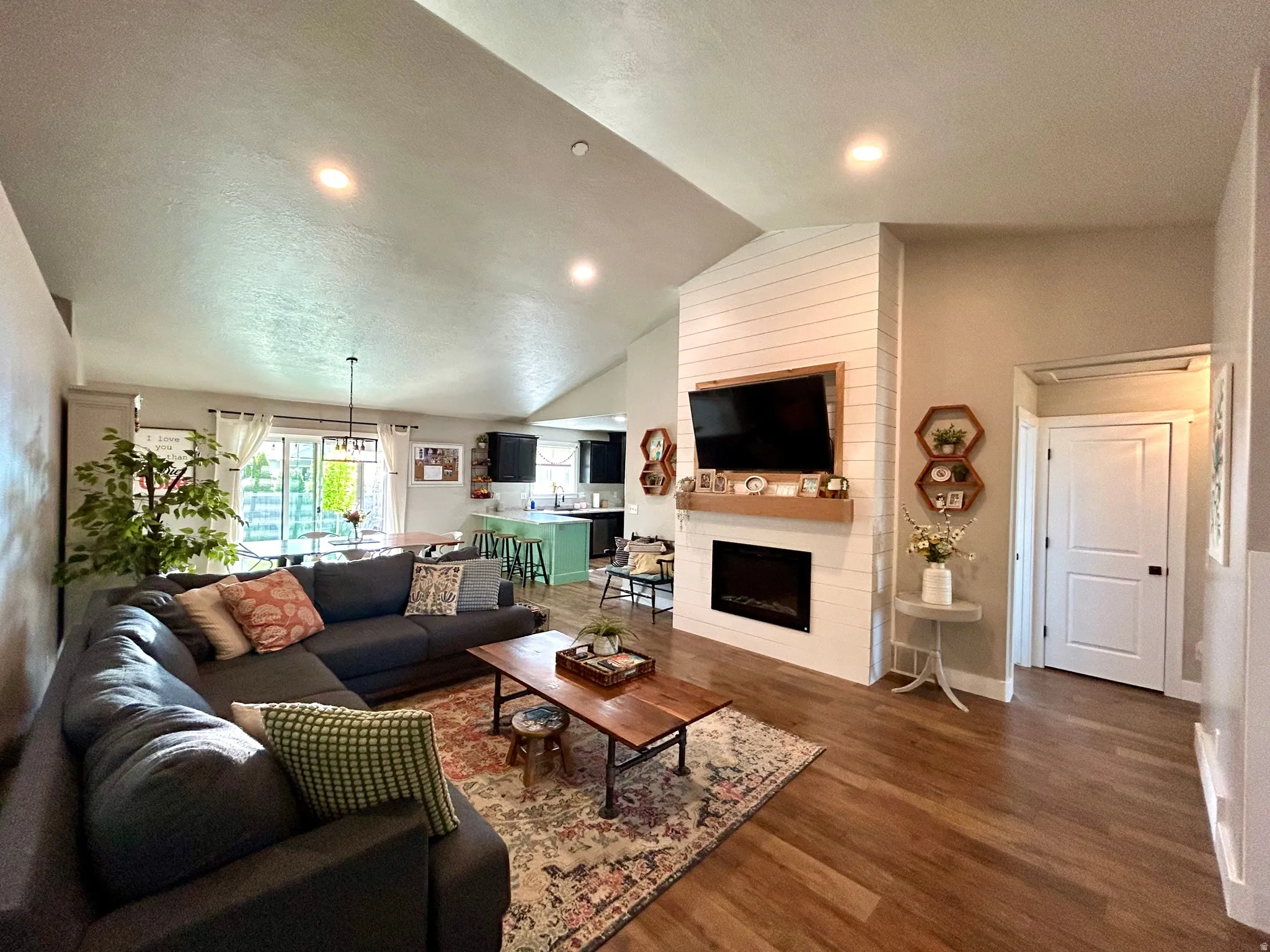 Vaulted living space featuring wood-finish flooring, recessed lighting, and a shiplap accent wall with a built-in fireplace
