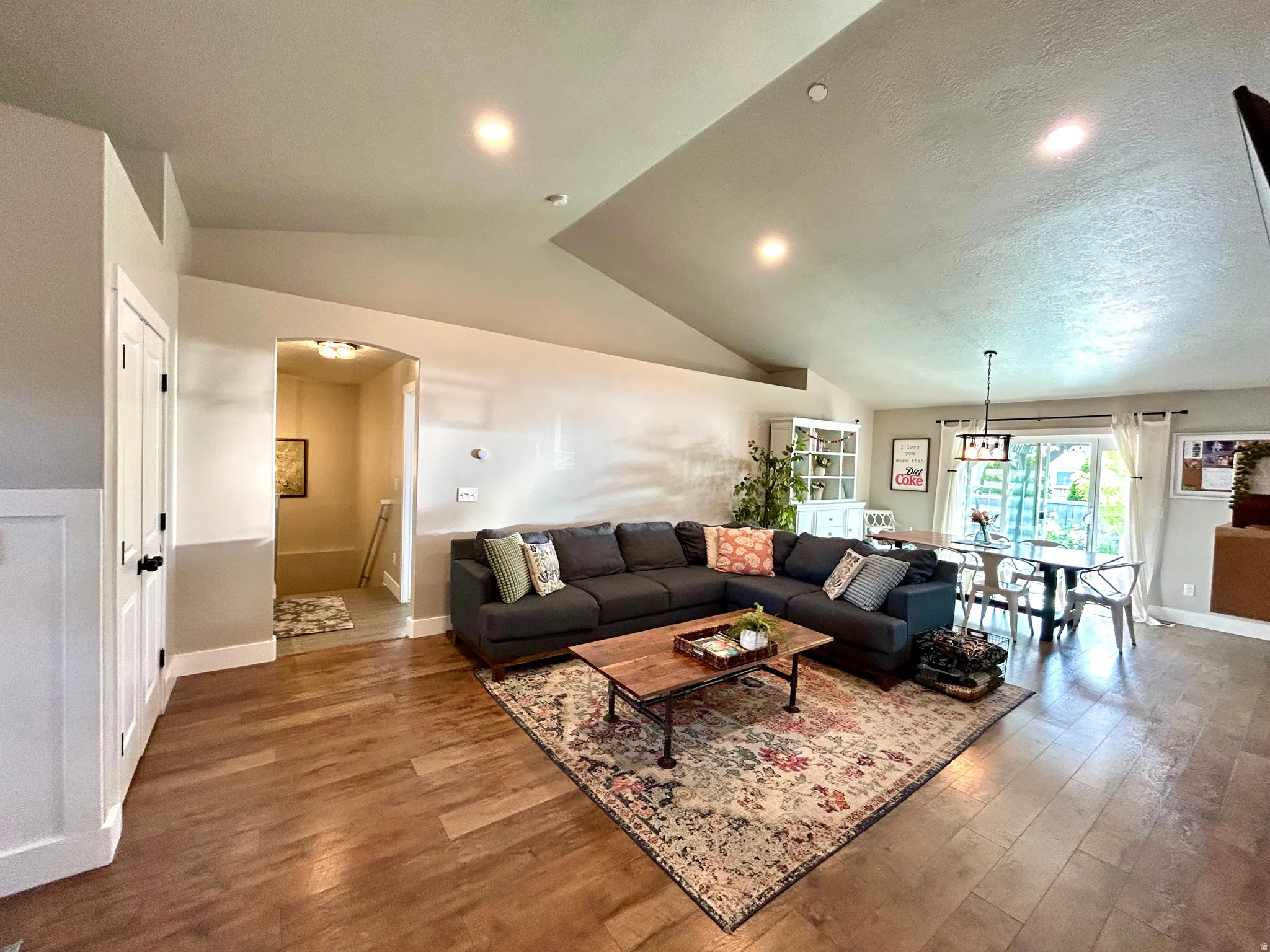 Open-concept living area featuring vaulted ceilings, wood-finish flooring, a dining area with a contemporary chandelier, and a sliding glass door