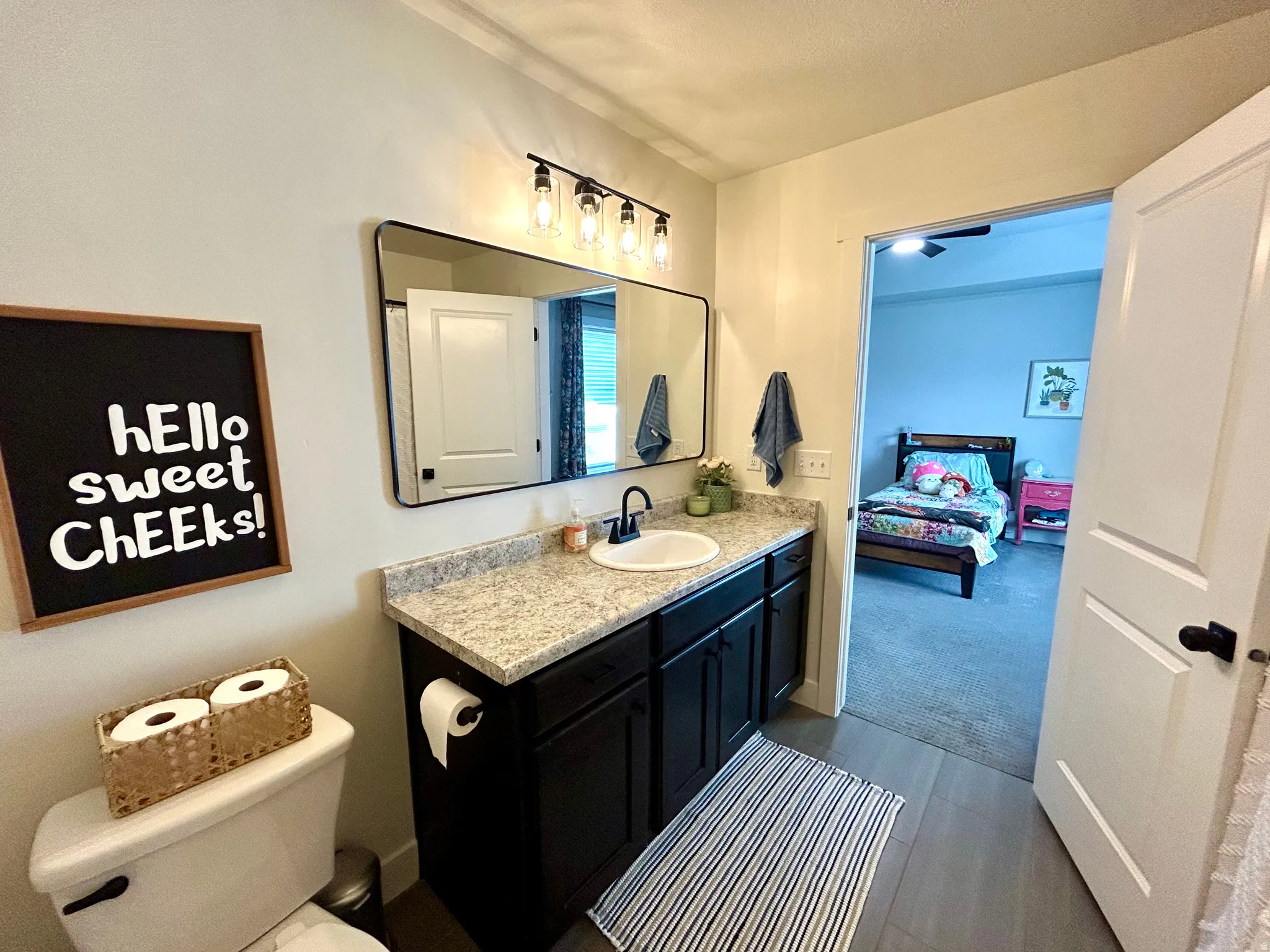 Bathroom vanity featuring a black cabinet with a light-colored countertop, a rectangular mirror, and a wall-mounted light fixture