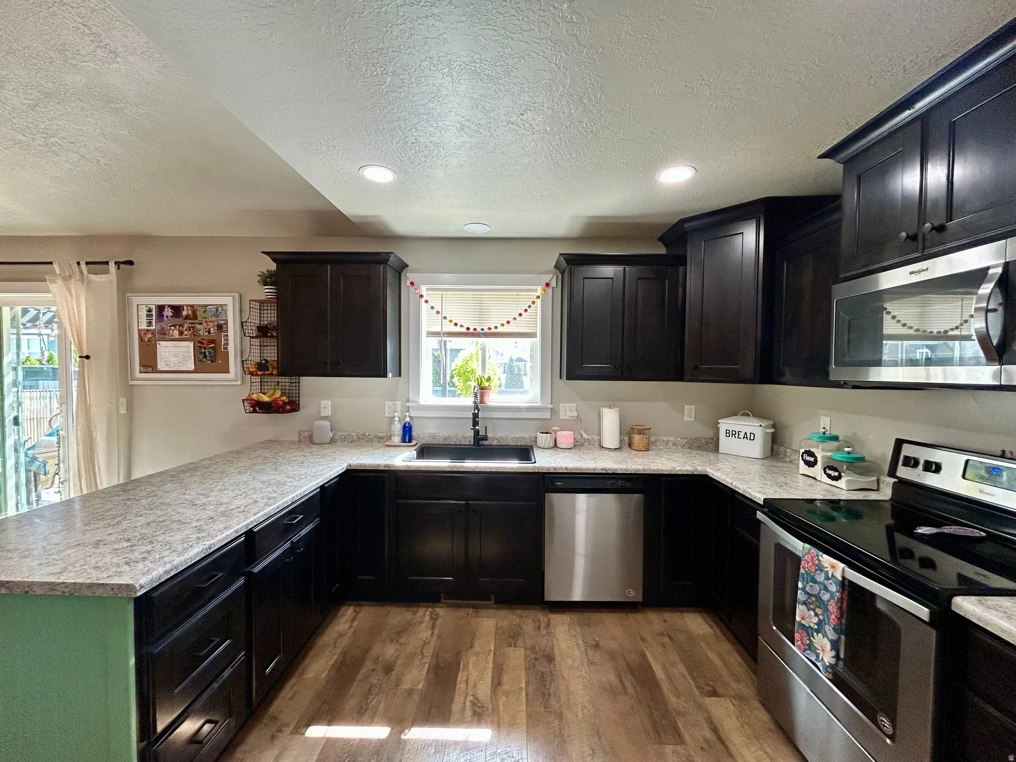 Spacious kitchen featuring dark wood cabinetry, light-toned countertops, stainless steel appliances, wood-finish flooring, and recessed lighting