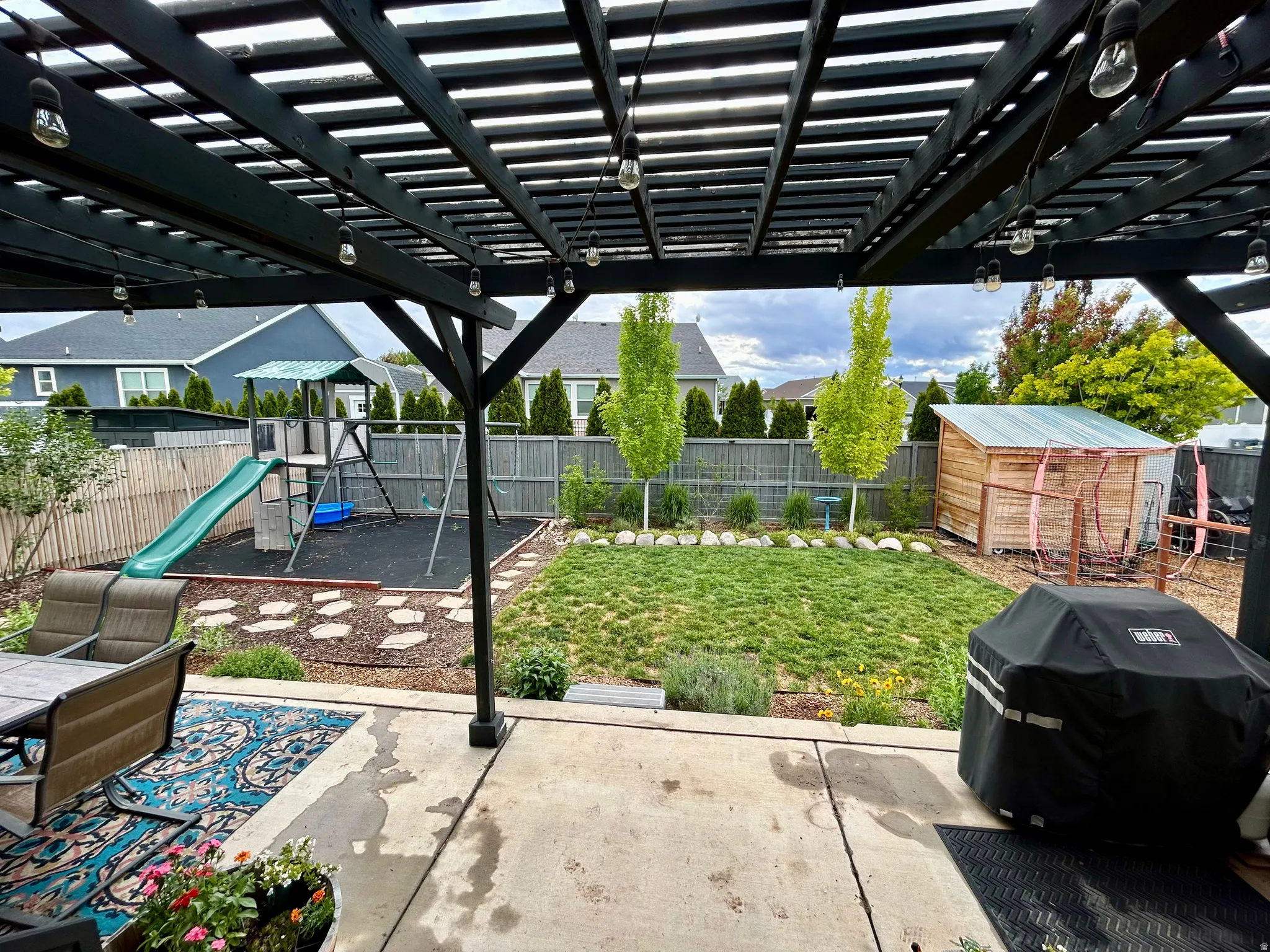 Spacious backyard featuring a concrete patio, dark wood pergola, and a manicured lawn