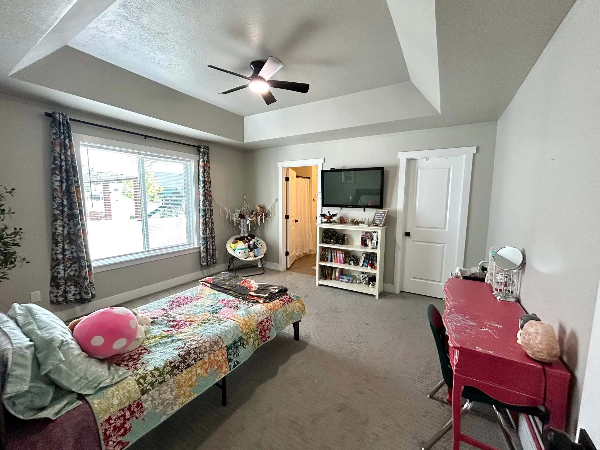 Carpeted interior room featuring a tray ceiling with a ceiling fan, a large window with white trim, and a white interior door with black hardware