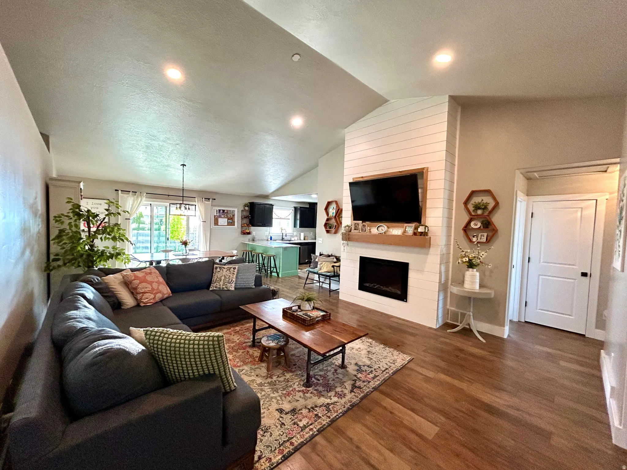 Living area featuring wood-finish flooring, a vaulted ceiling with recessed lighting, and a fireplace with a shiplap surround and wood mantel