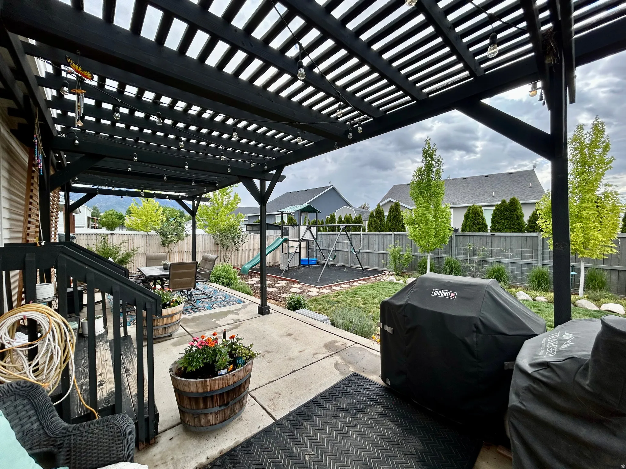 Expansive concrete patio featuring a black wooden pergola with string lighting