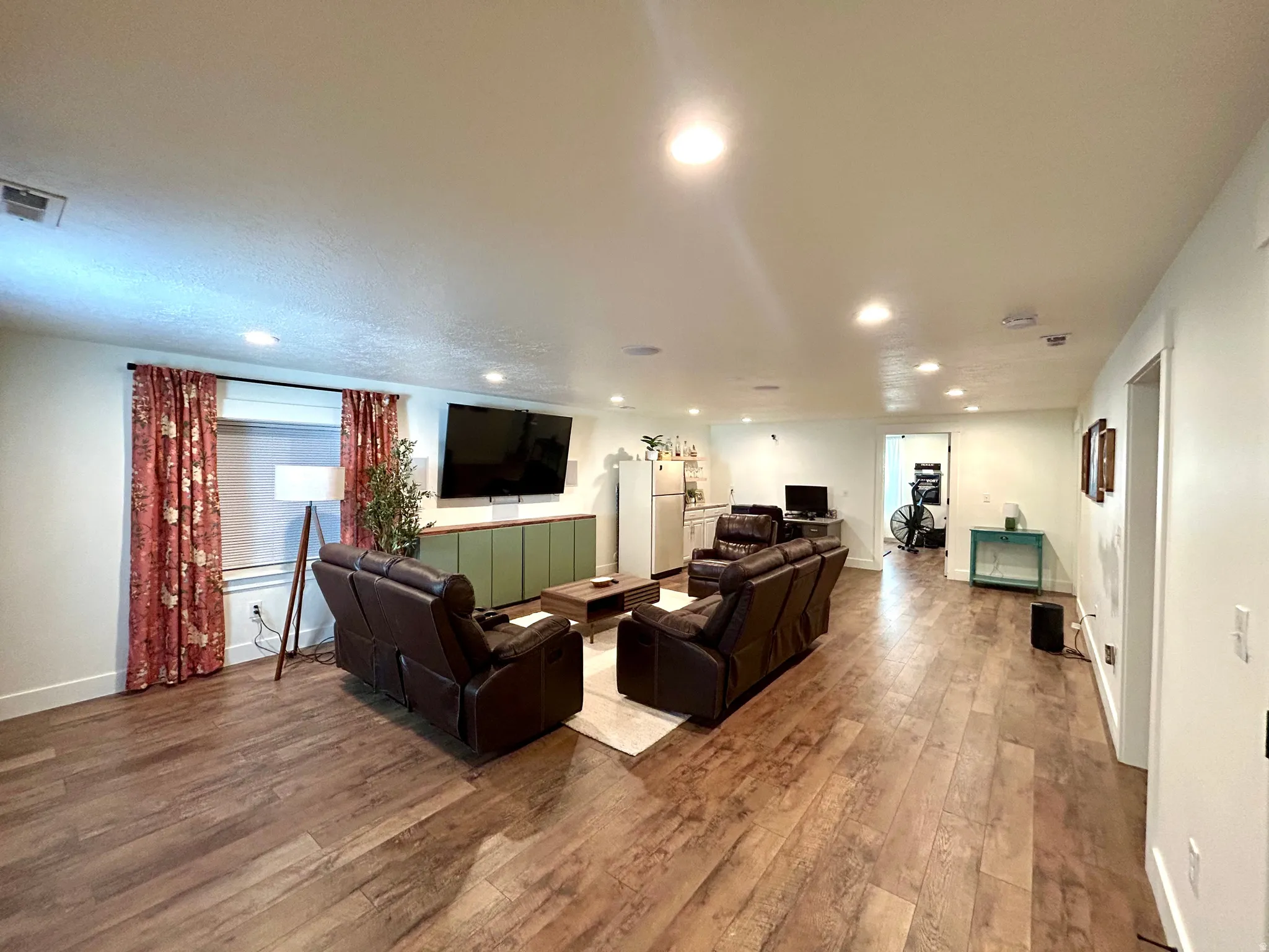 Spacious living area featuring wood-finish flooring, recessed lighting, white walls, and a built-in green cabinet unit