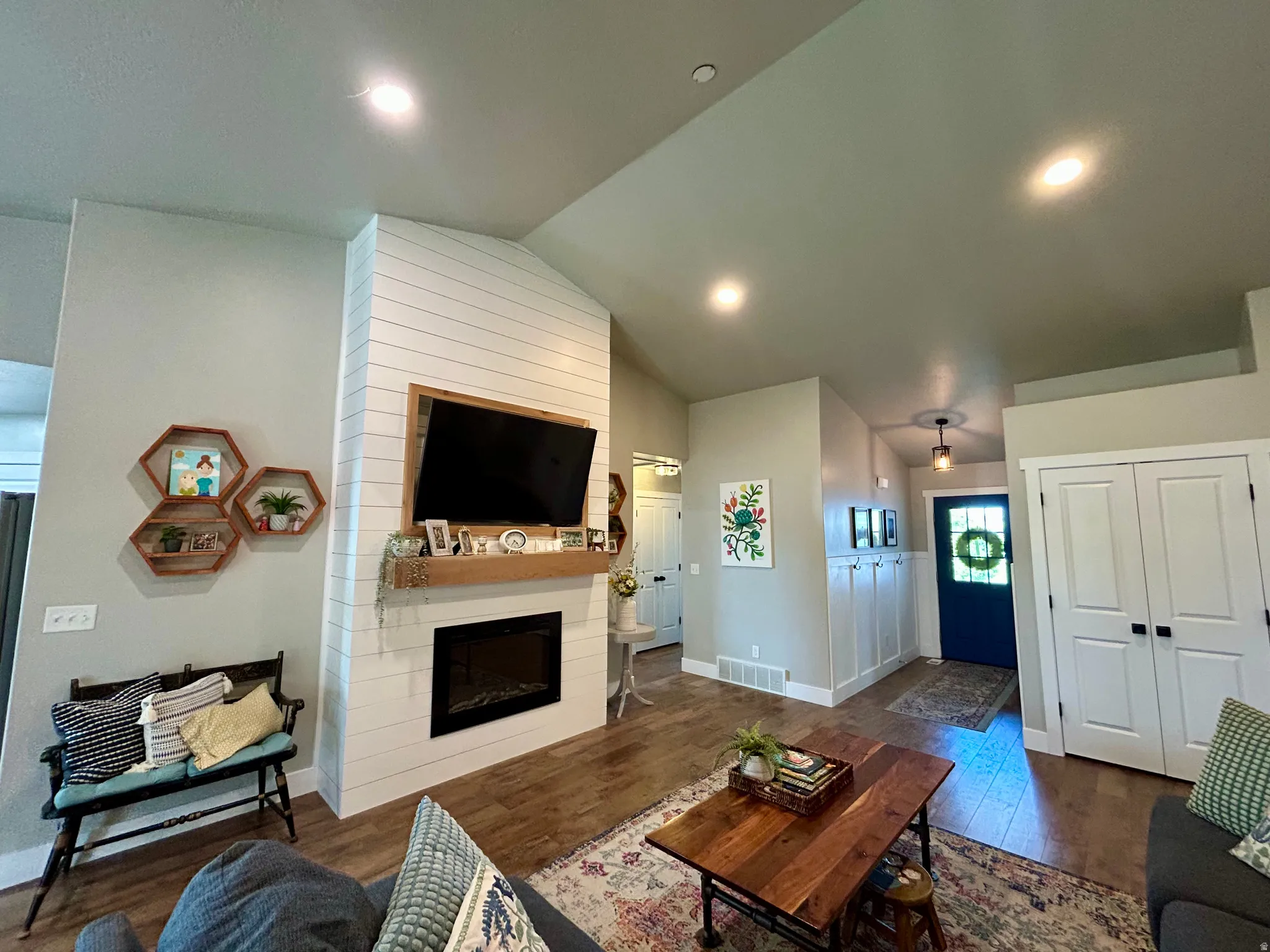 Living space with wood-finish flooring, a vaulted ceiling with recessed lighting, and a shiplap fireplace with an electric insert and wood mantle