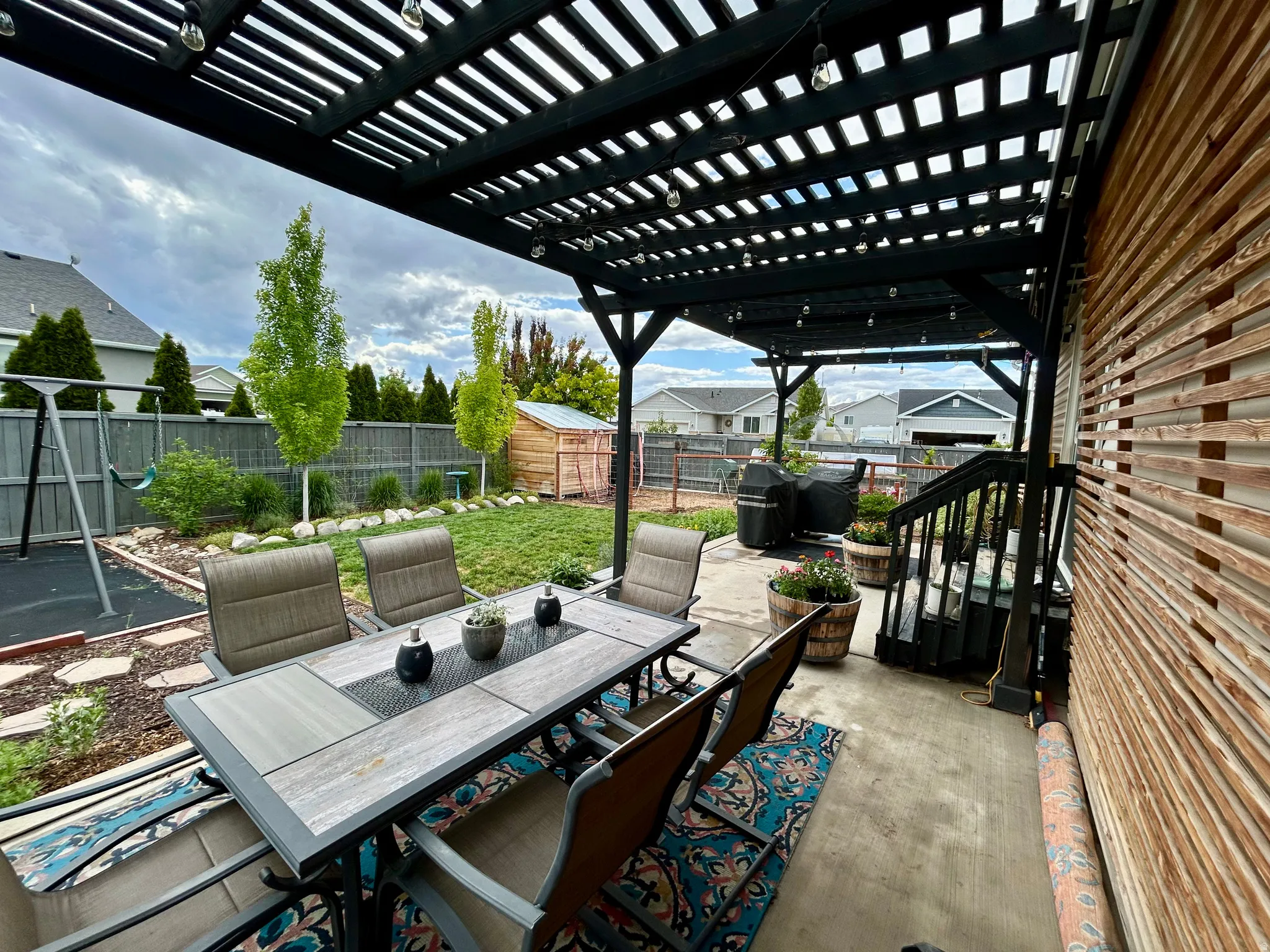 Covered patio featuring a black slatted pergola and string lighting